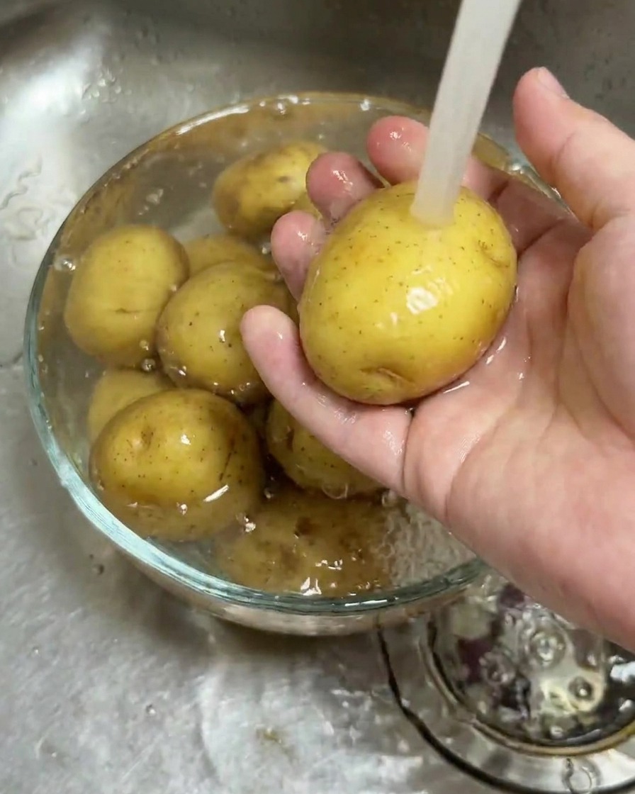Petites pommes de terre nettoyées dans un bol en verre sous un filet deau courante.