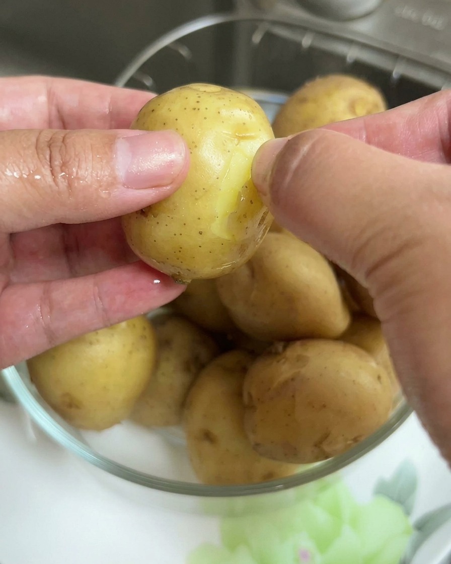 Gros plan de mains retirant la fine peau dune petite pomme de terre bouillie.