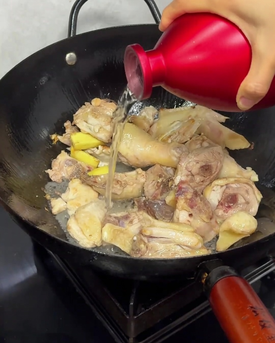 Filet de vin de riz versé sur les morceaux de poulet en train de saisir dans le wok.