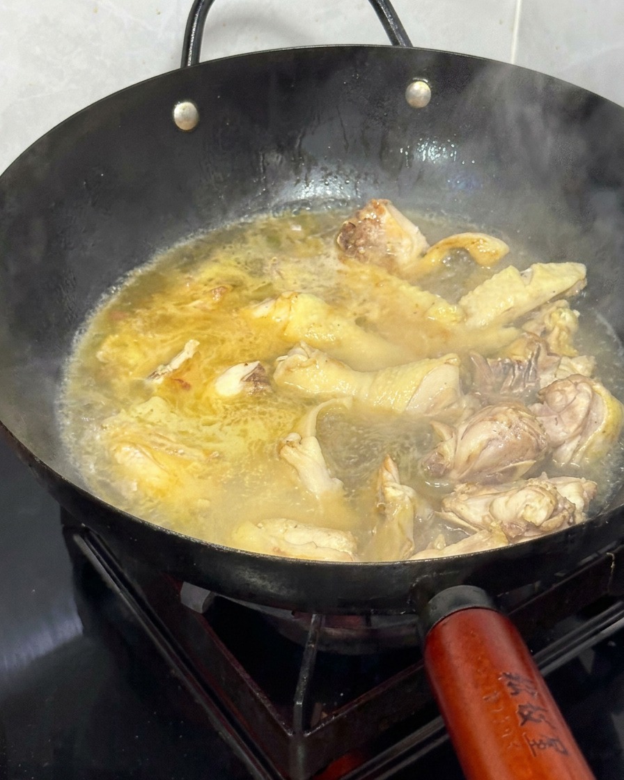 Eau chaude versée dans le wok contenant le poulet sauté et le gingembre.