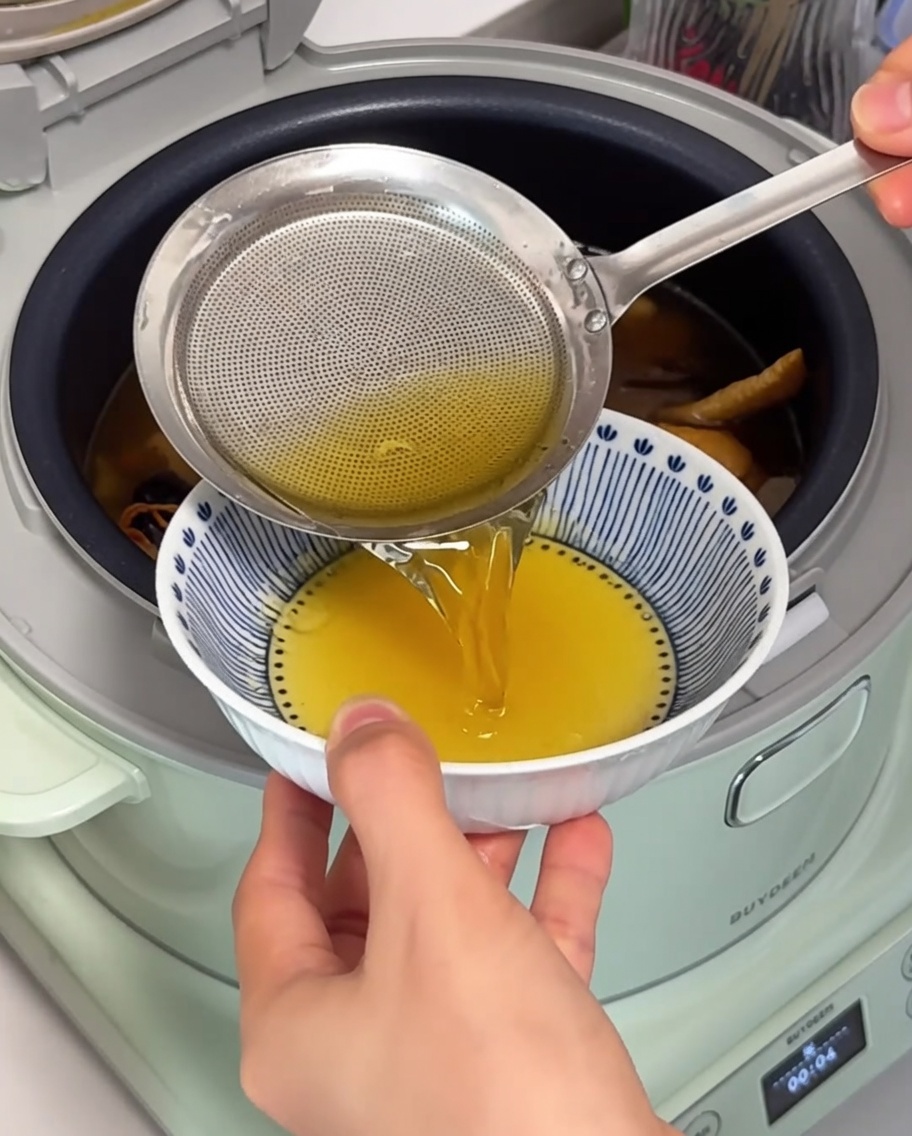 Gros plan sur une passoire fine retirant lhuile de poulet dorée et limpide à la surface de la soupe frémissante.