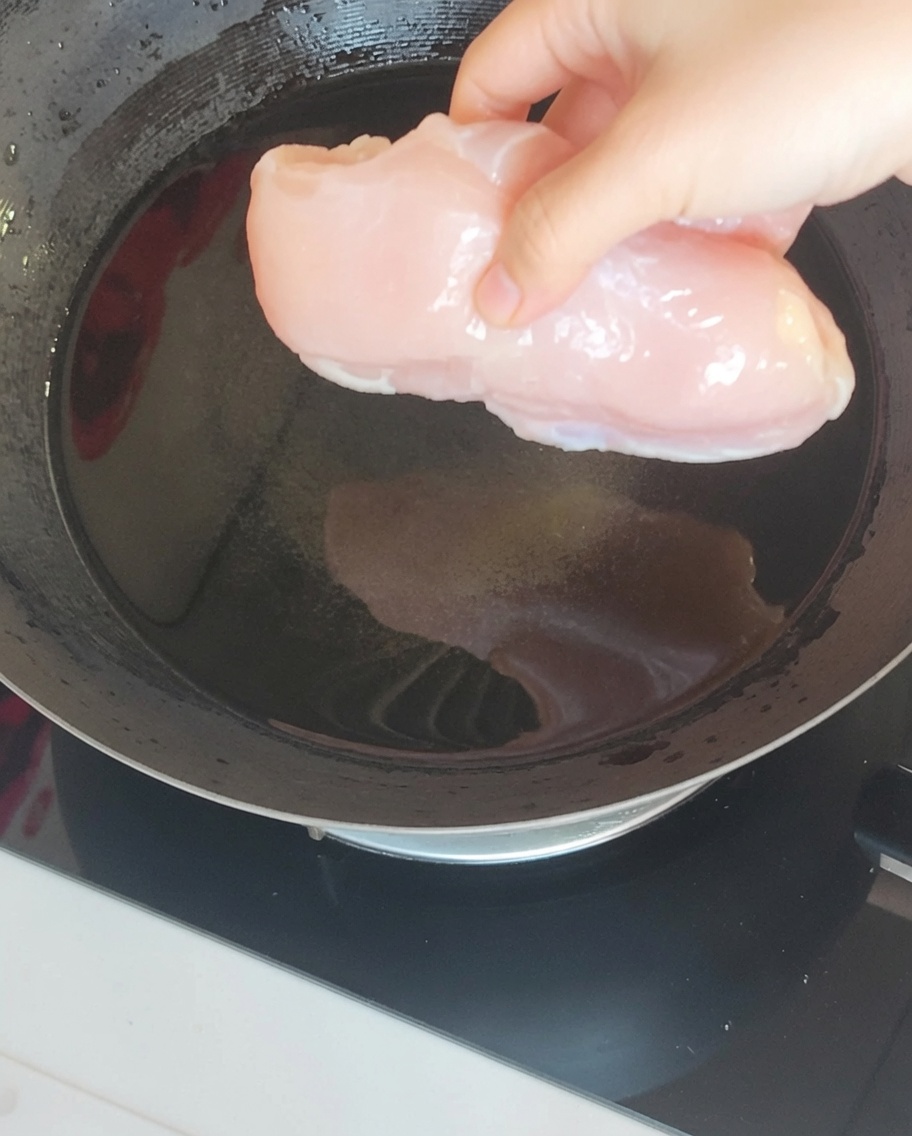 Un blanc de poulet immergé dans de leau bouillante dans un wok avec du gingembre et de loignon vert.