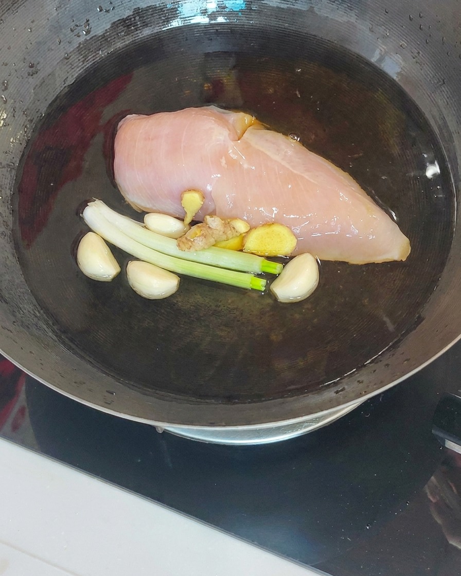 Blanc de poulet cuit soulevé dun wok à laide dune écumoire et de baguettes.
