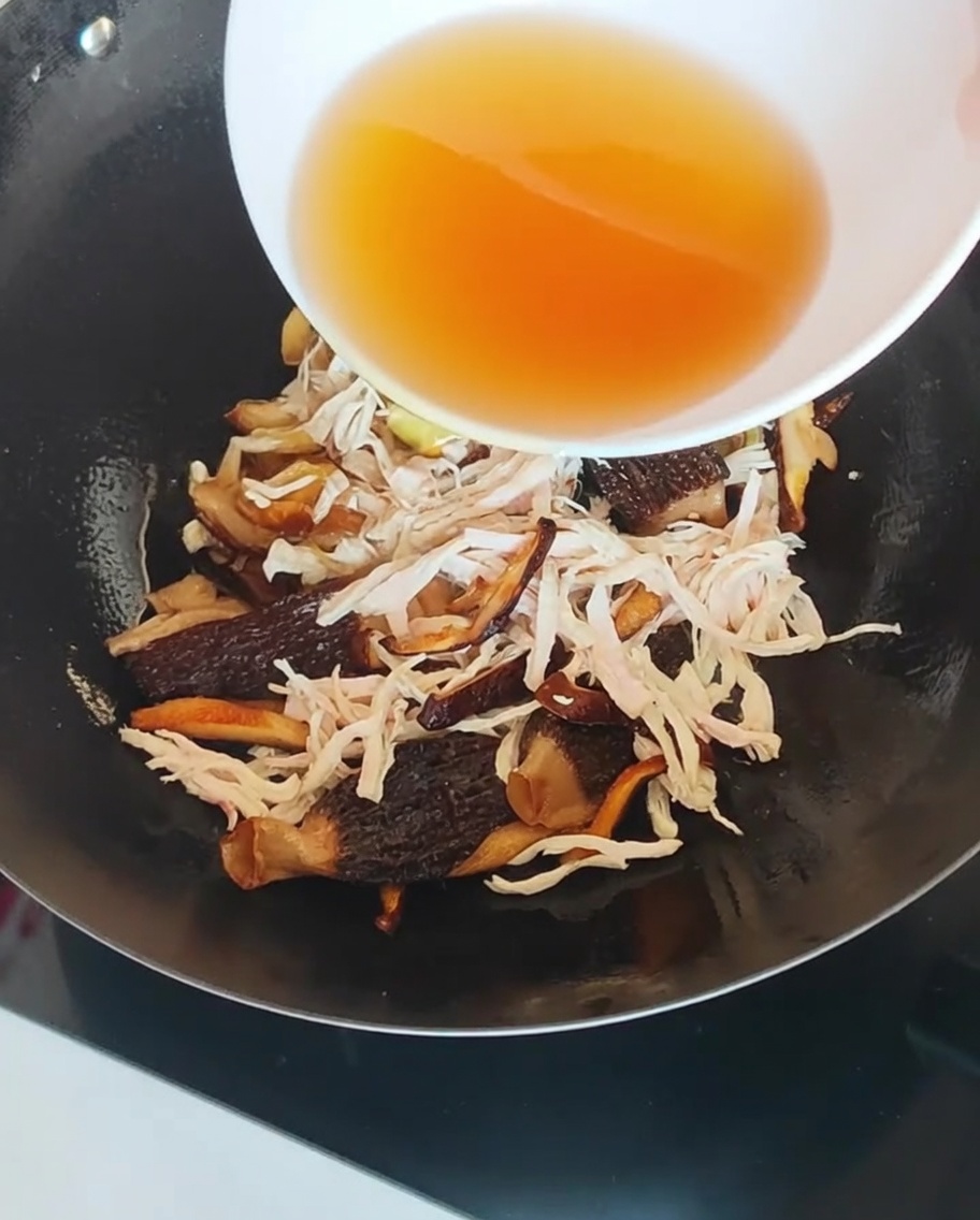 Liquide de trempage des champignons ambré versé dans un wok contenant poulet et champignons.