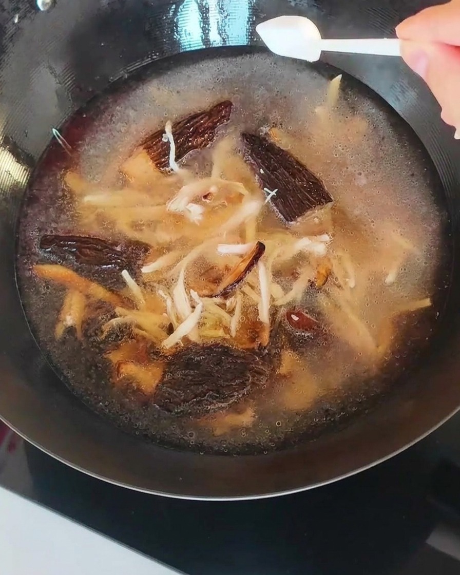 Le bouillon dans la poêle, contenant champignons et poulet effiloché, assaisonné dune cuillerée de sel.