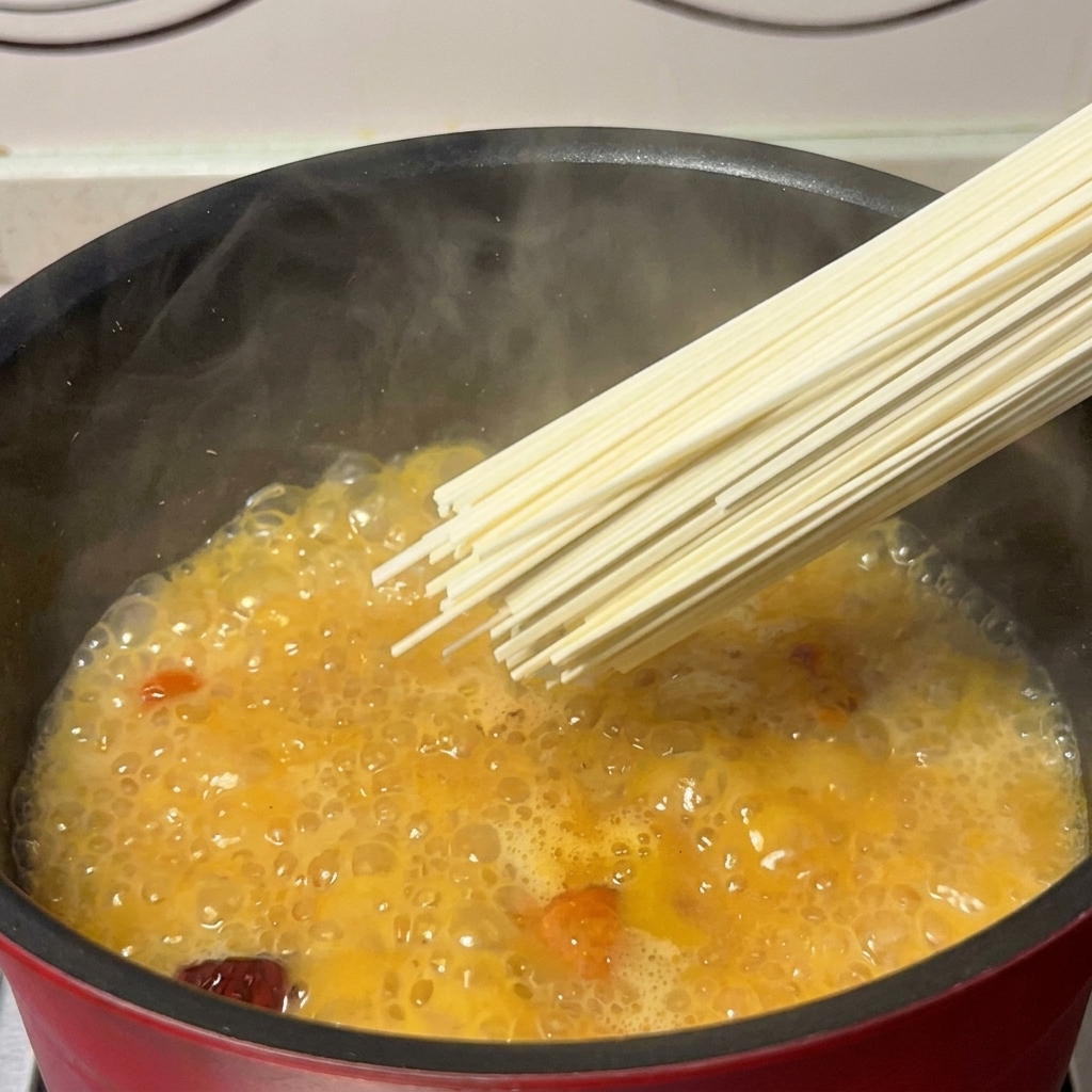 Une poignée de nouilles sèches plongées dans une casserole de bouillon de poulet et de champignons doré et frémissant.