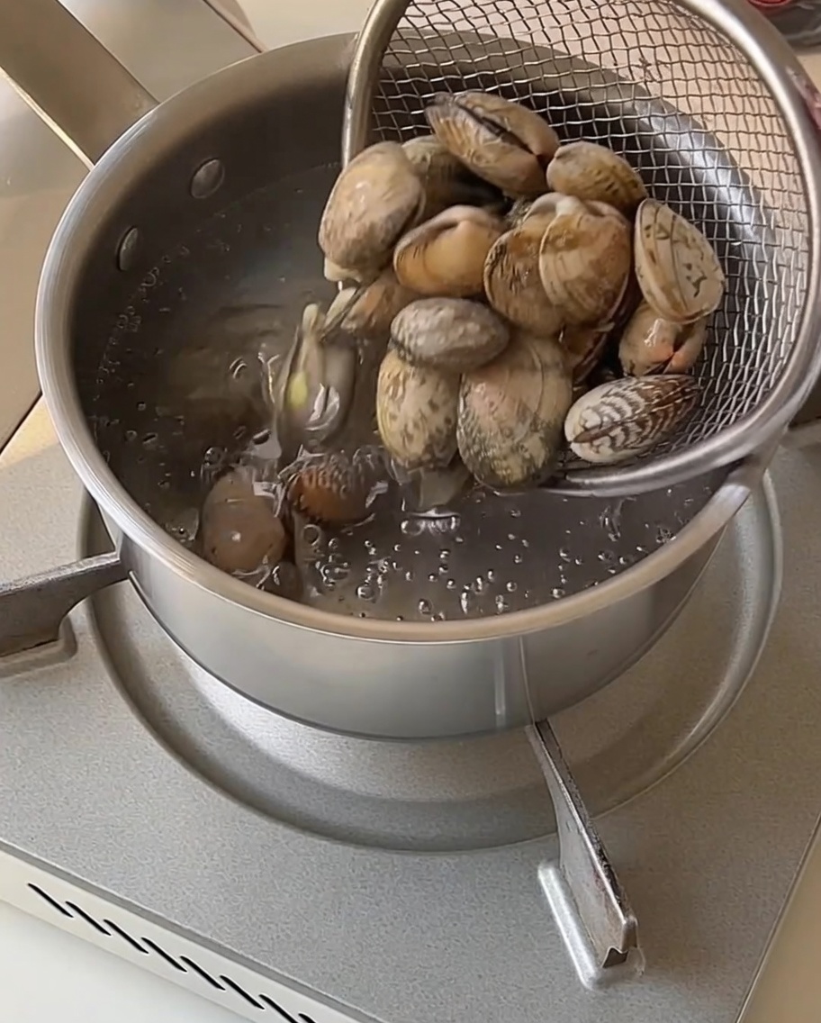 Des palourdes dans une passoire en filet retirées dune casserole deau bouillante.