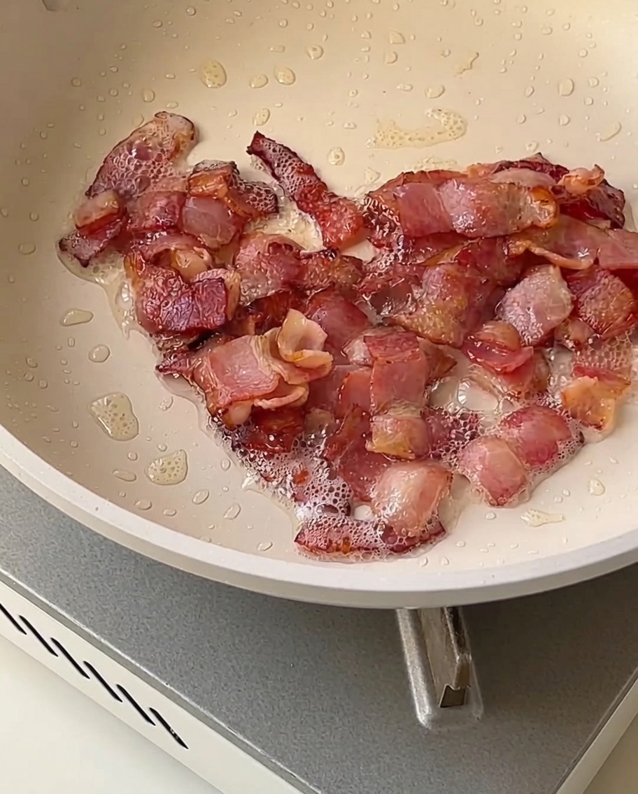 Cubes doignon, de céleri et de pomme de terre rissolant dans une poêle avec des morceaux de lardons dorés et croustillants.