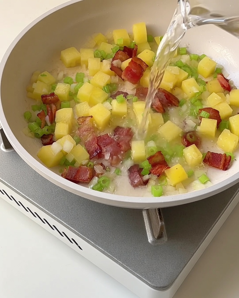 Du bouillon de palourdes clair versé dans une poêle contenant le mélange de légumes sautés et de lardons.