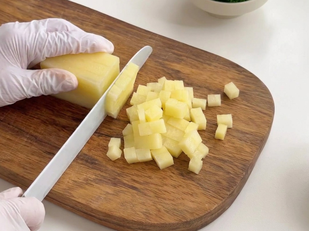 Pommes de terre pelées coupées en petits dés uniformes sur une planche en bois.