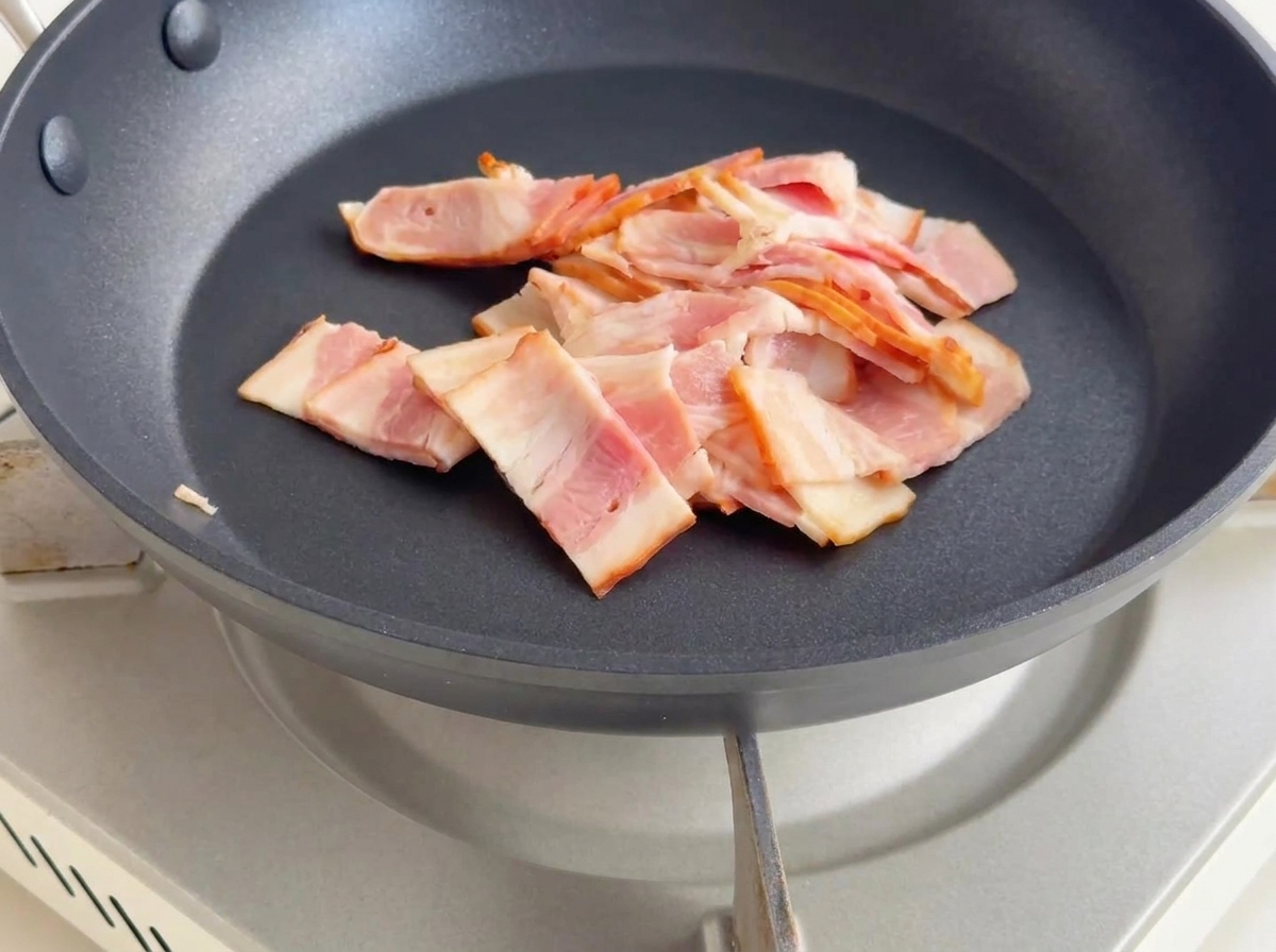 Morceaux de bacon frits dans une poêle, devenant dorés et libérant leur gras.