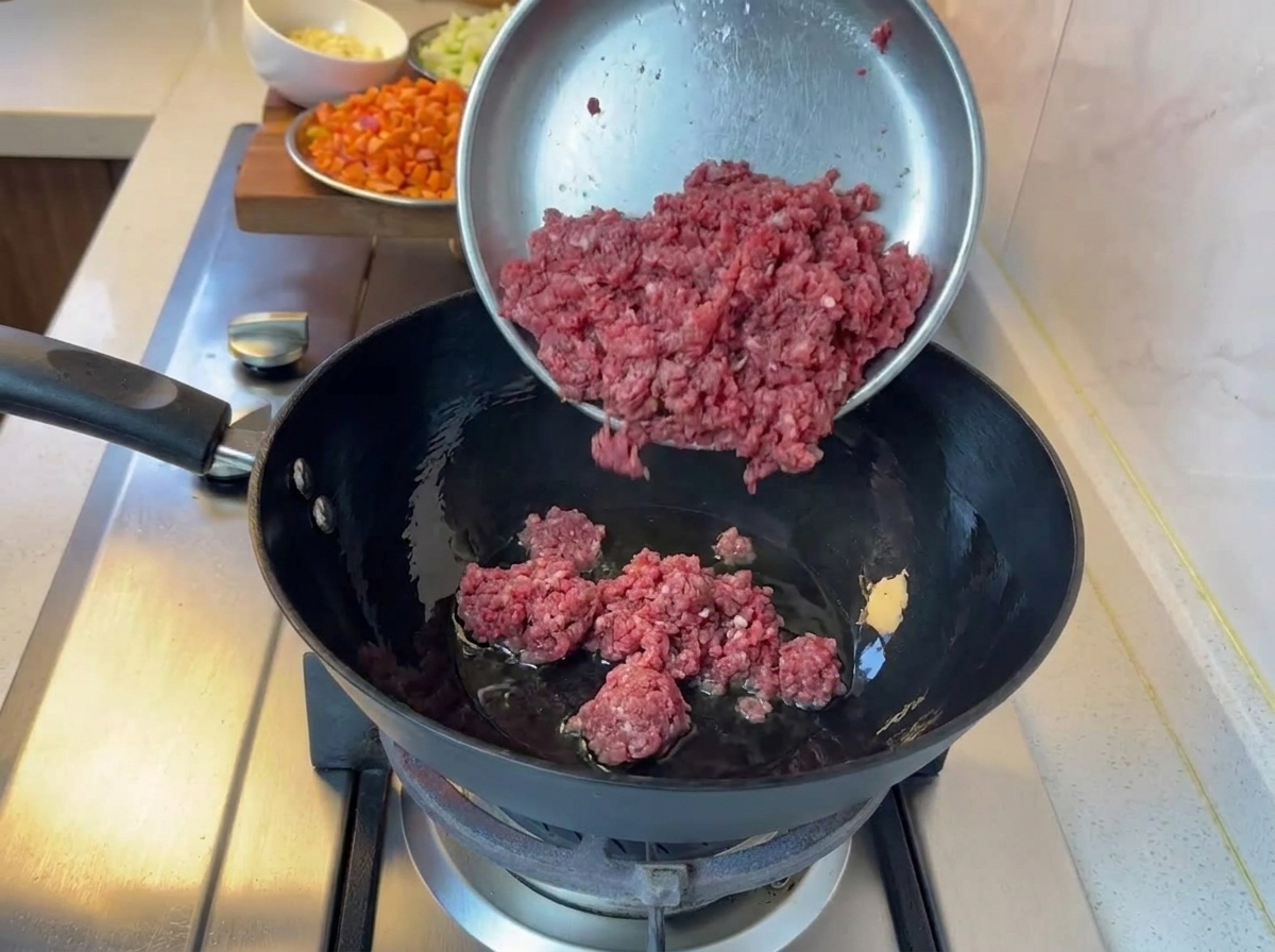 Bœuf haché en cours de cuisson dans une poêle noire sur une gazinière.