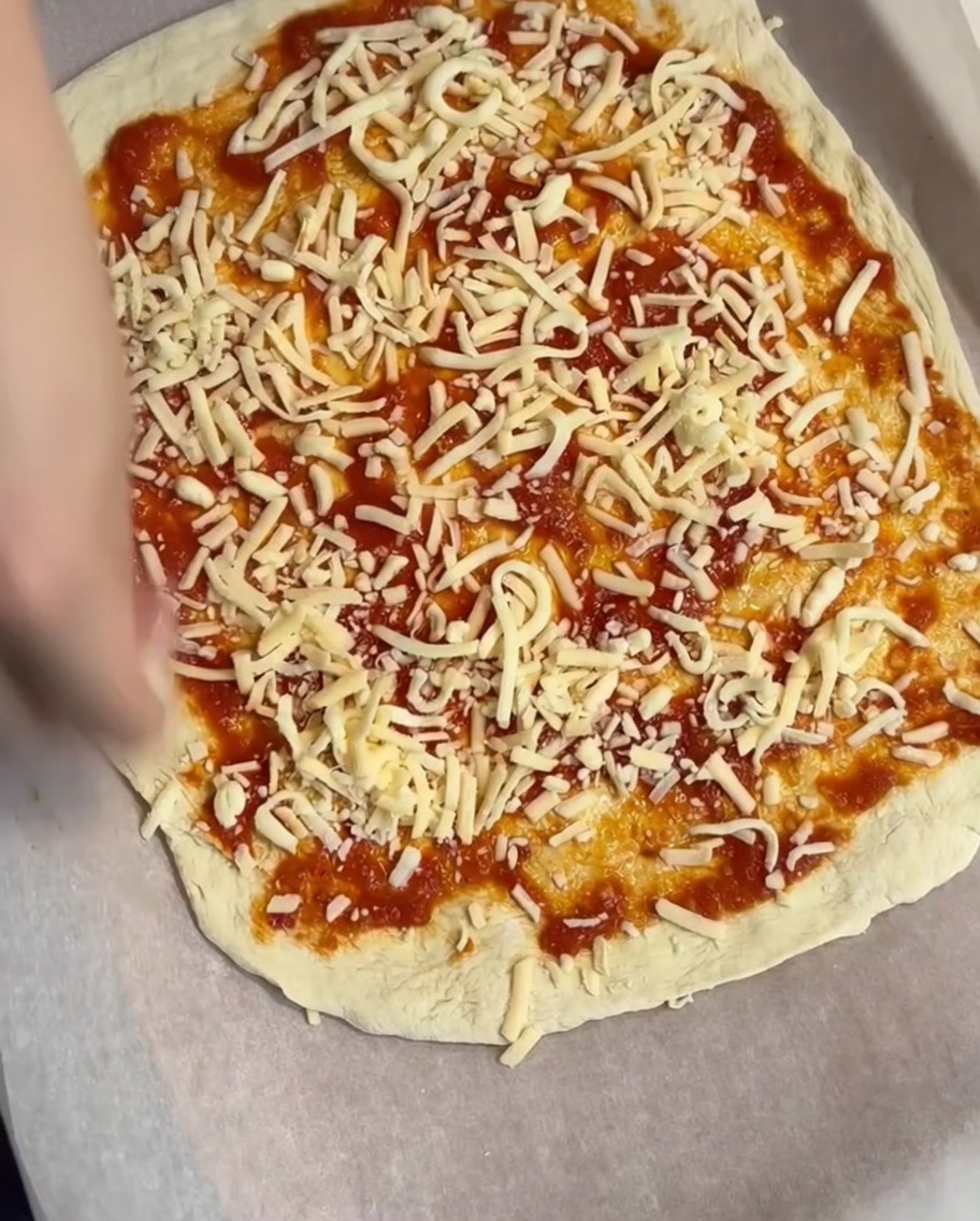 Une couche de fromage râpé saupoudrée sur la base de sauce tomate.