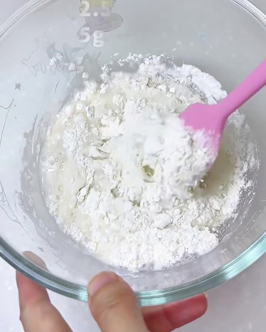Ingrédients pour la pâte à pizza mélangés dans un grand bol en verre avec une spatule en silicone.
