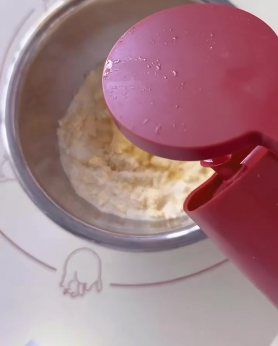 Huile de cuisson versée dans le bol mélangeur contenant la farine et lœuf.
