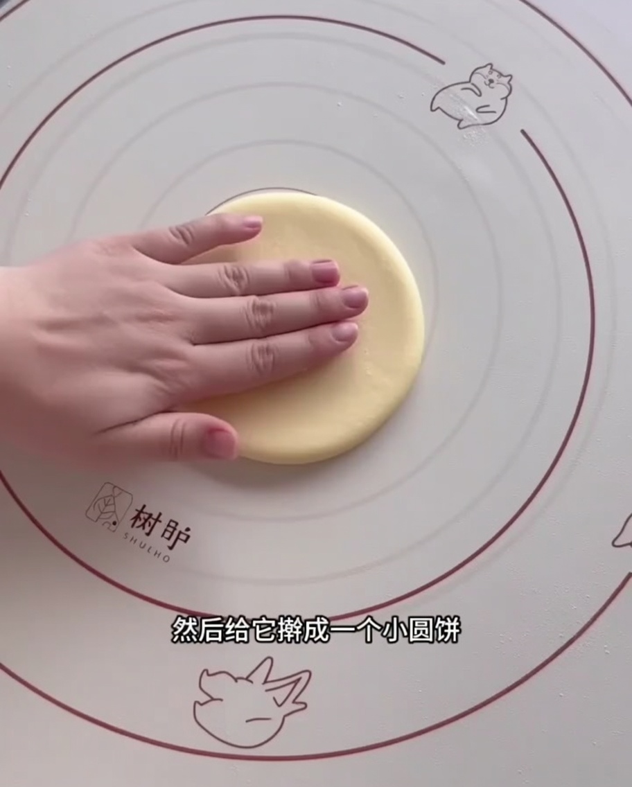 Une portion de pâte aplatie en cercle à laide dun rouleau à pâtisserie en bois sur un tapis en silicone.
