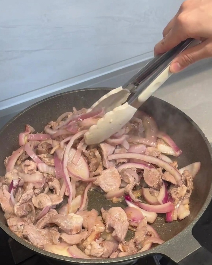 Sauce épicée versée sur le porc et les oignons dans la poêle.