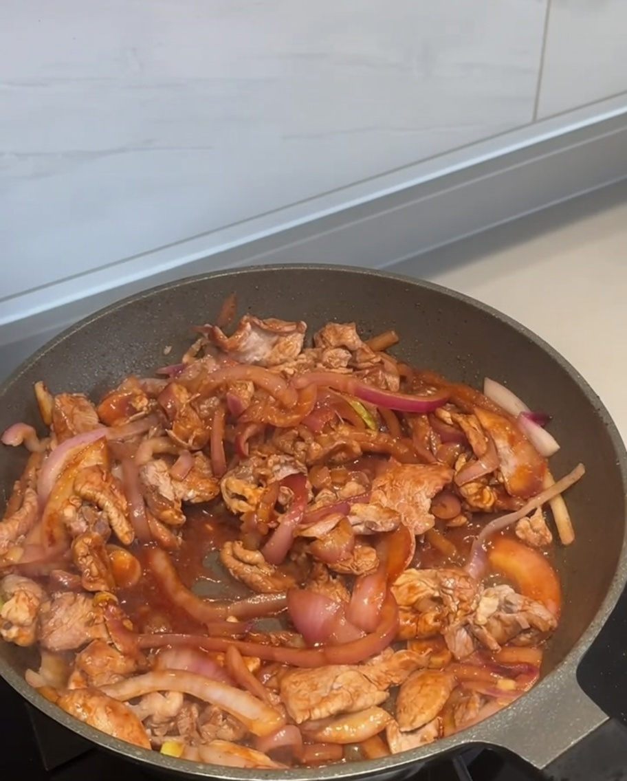 Piment en poudre saupoudré sur le porc et les oignons en train de cuire.