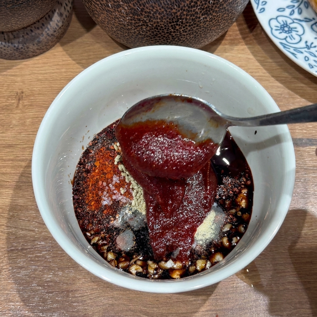 Un bol blanc contenant une sauce rouge épaisse avec de lail et des flocons de piment.
