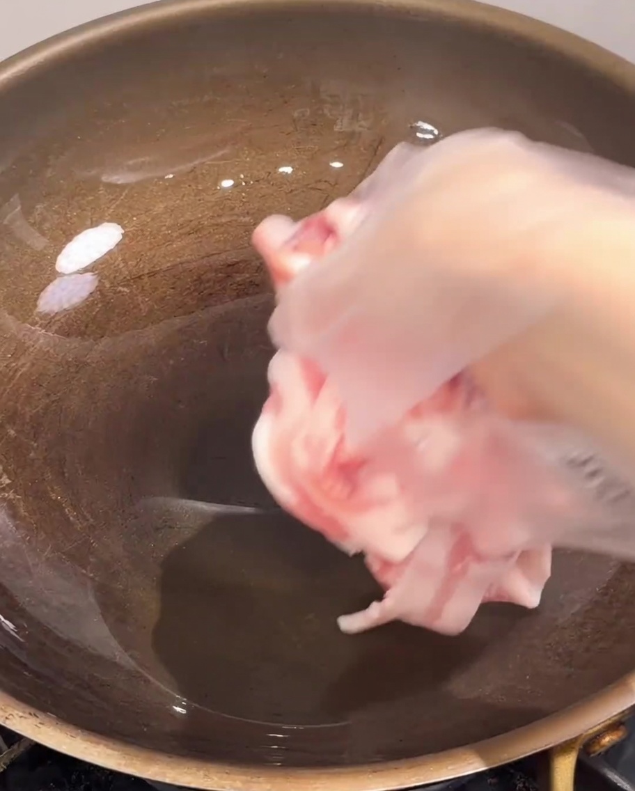 Tranches de poitrine de porc déposées dans une poêle chaude.