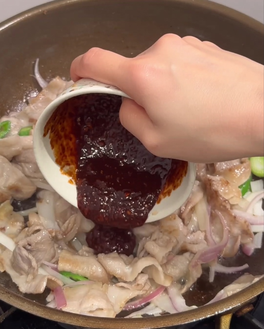 La sauce rouge versée sur le porc et les légumes dans la poêle.