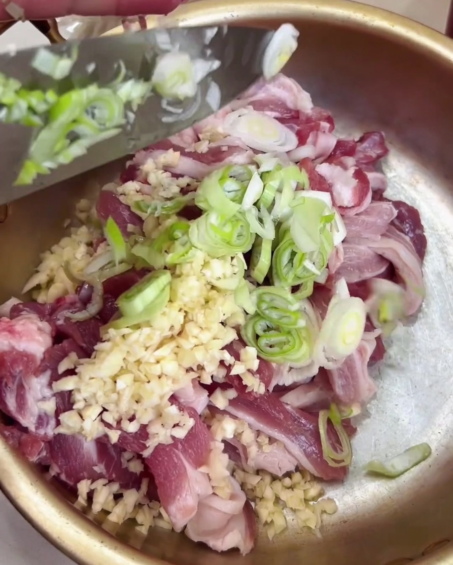 Oignons verts hachés ajoutés au bol de porc en métal.