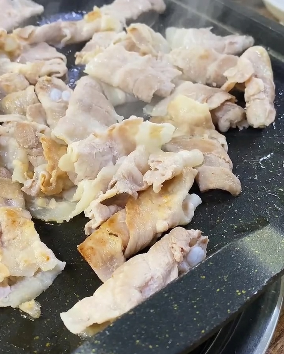 Tranches de poitrine de porc dorées et croustillantes cuisant sur la plaque du gril.