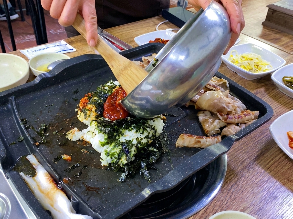 Riz, légumes et un œuf versés sur la plaque du gril chaude à côté du porc cuit.