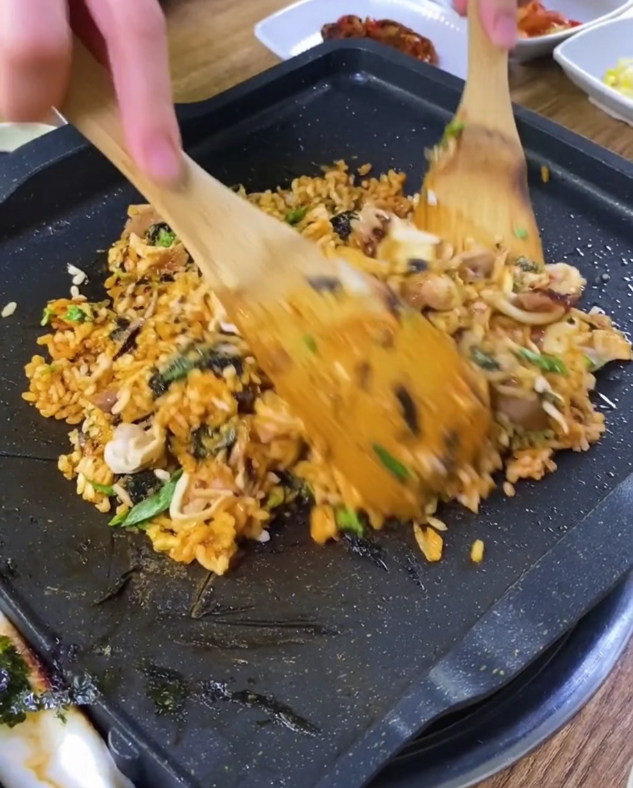 Gros plan de spatules en bois mélangeant de la poitrine de porc grillée hachée avec du riz sauté et des légumes sur un gril chaud.