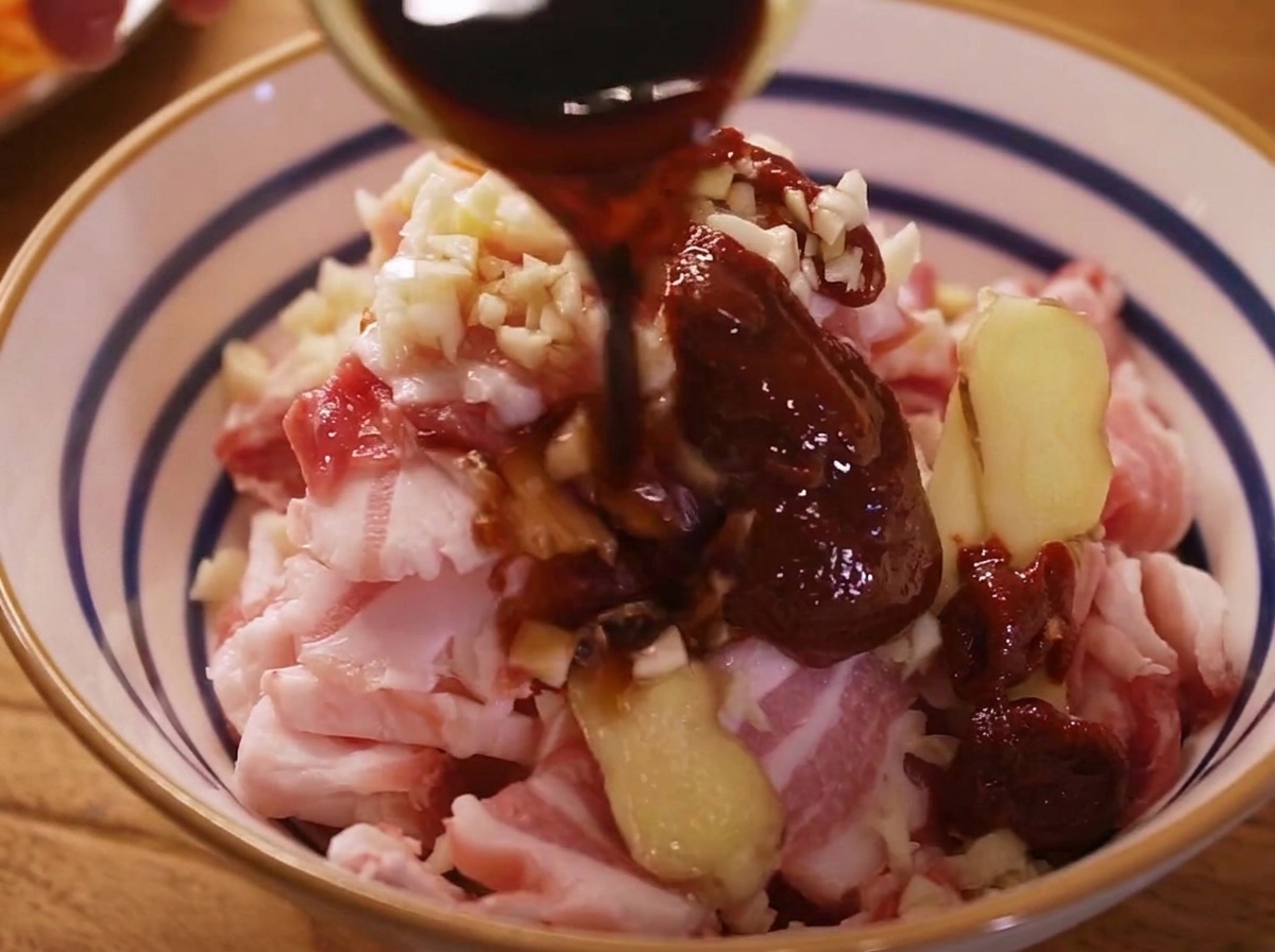 Gros plan sur des bandes de poitrine de porc en train dêtre massées avec une marinade rouge intense dans un bol.