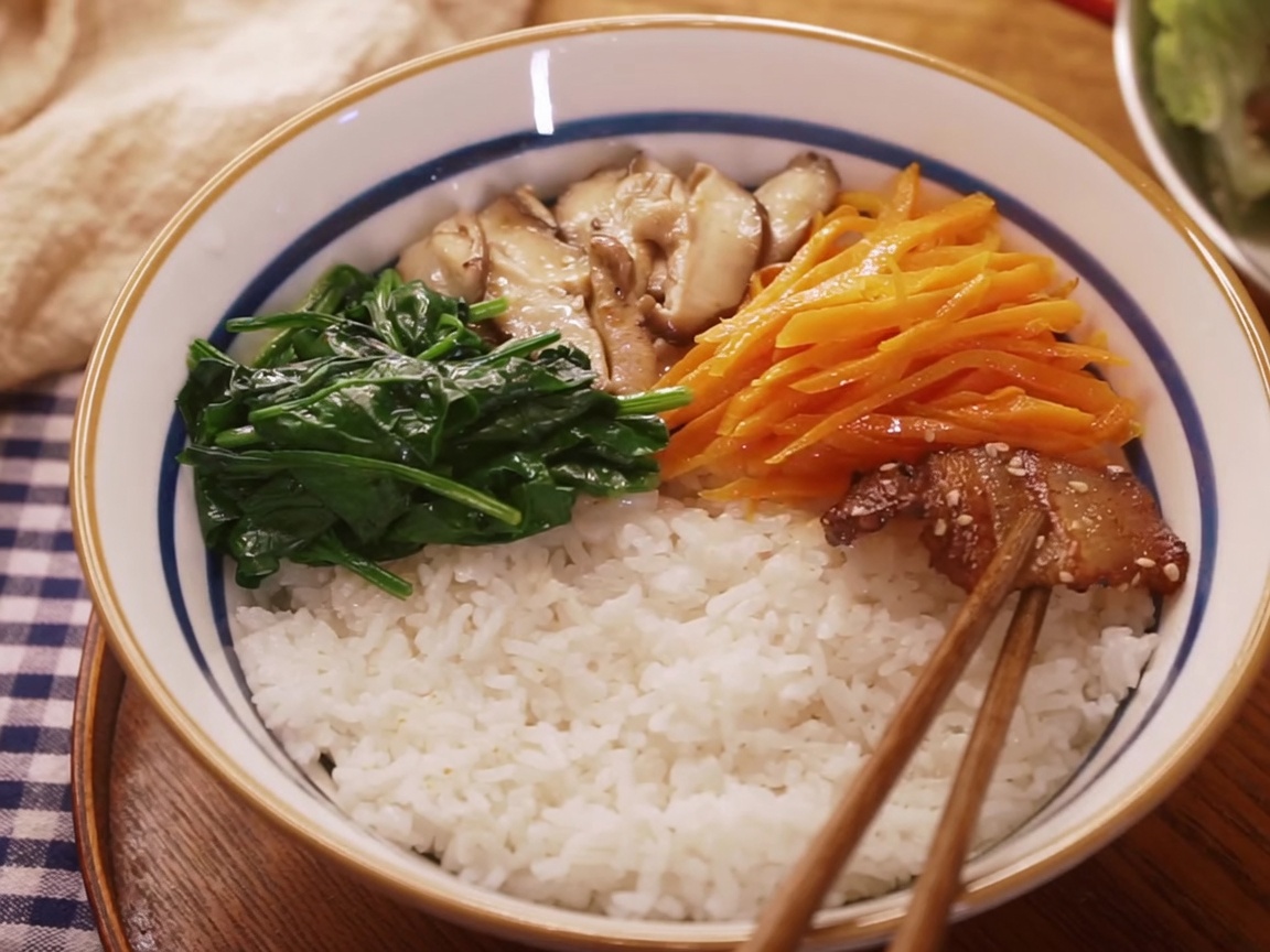 Vue de dessus des ingrédients du bibimbap assemblés et disposés soigneusement sur un lit de riz blanc dans un bol en céramique.