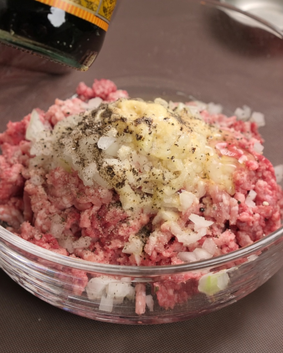 Sauce Worcestershire versée sur la viande, les oignons et les assaisonnements dans un bol.