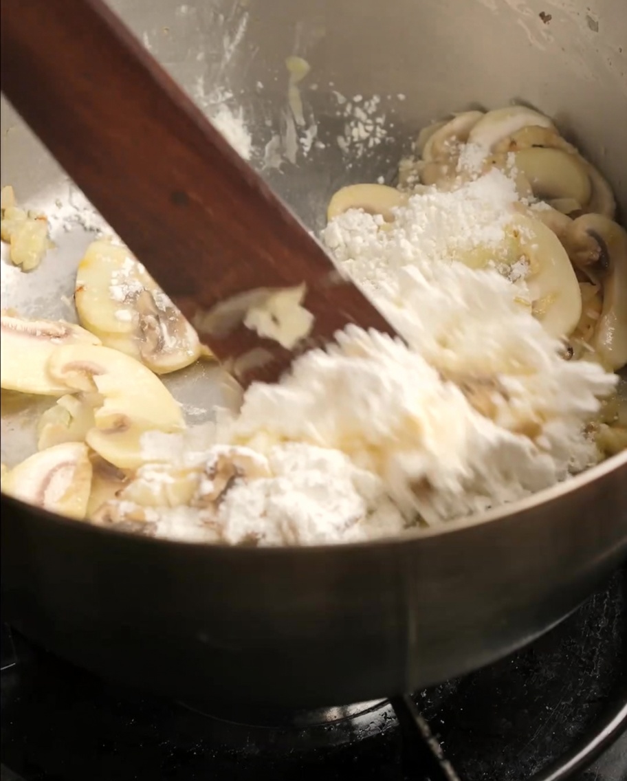 Farine incorporée aux champignons et oignons dans la poêle avec une spatule.
