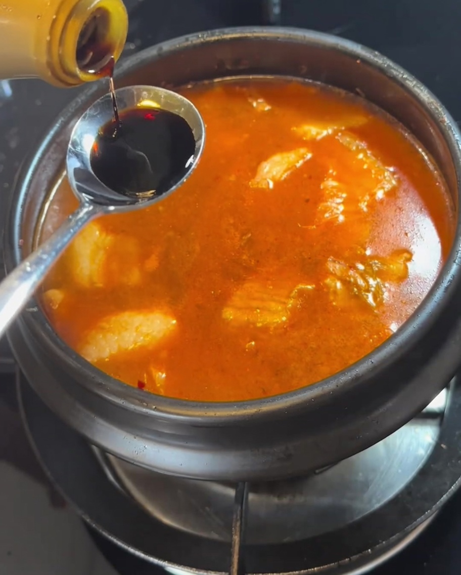 Une cuillère de sauce soja ajoutée au ragoût bouillonnant.