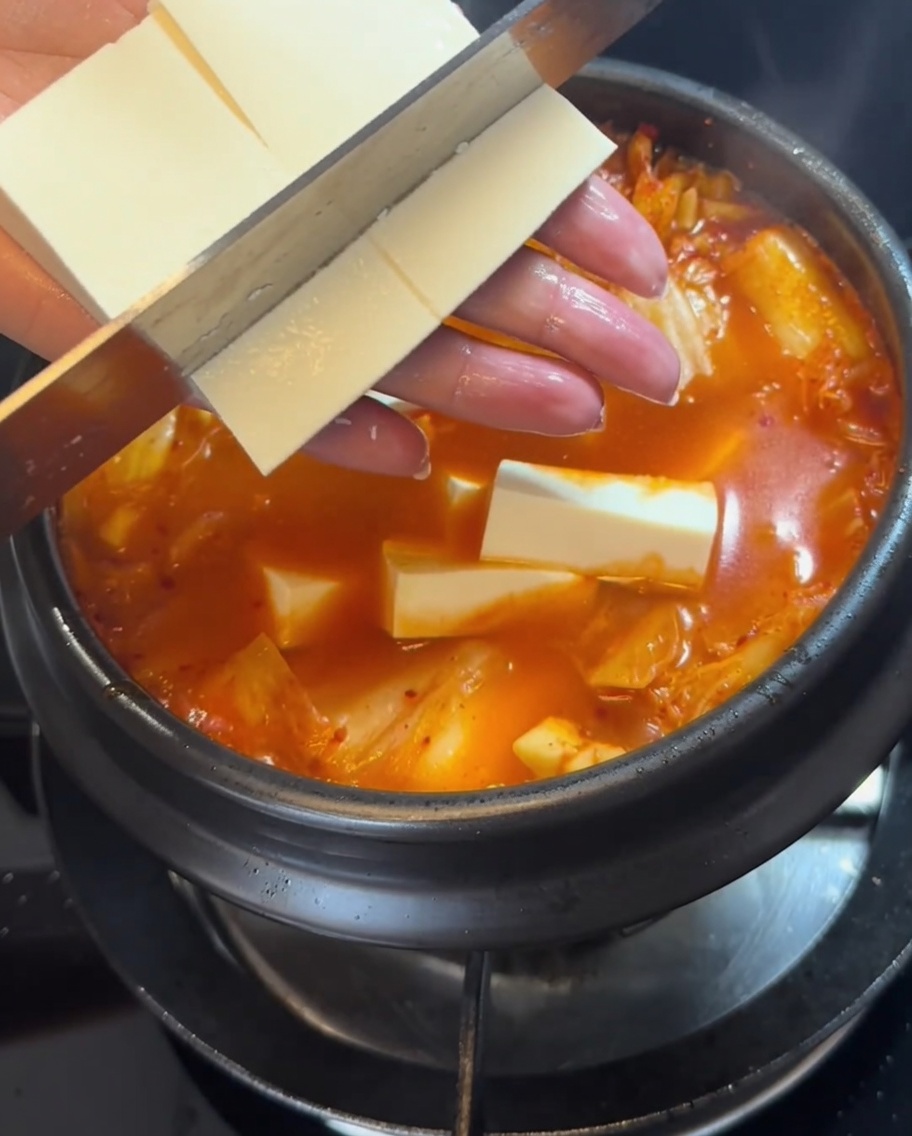 Tranches de tofu ferme délicatement placées dans le ragoût rouge bouillonnant.