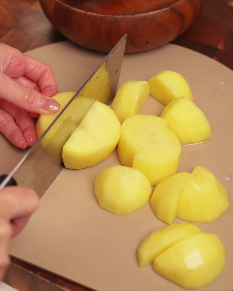 Pommes de terre pelées coupées en gros morceaux réguliers sur une planche à découper.