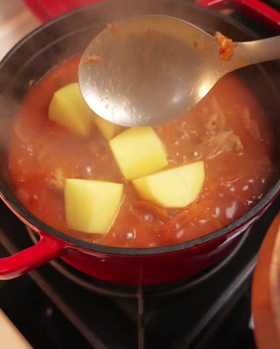 Morceaux de pommes de terre ajoutés dans une cocotte de ragoût de porc au kimchi frémissant.