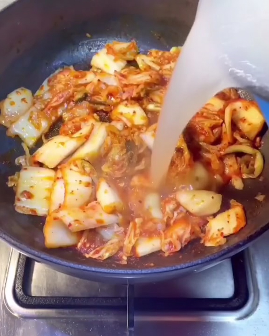 Bouillon de travers de porc versé dans une poêle contenant le kimchi sauté.