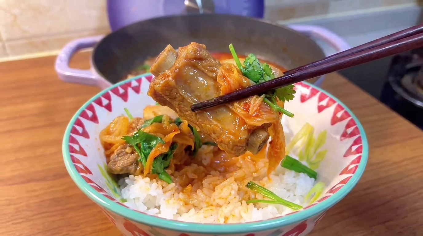 Un travers de porc tendre et du kimchi vibrant soulevés avec des baguettes au-dessus dun bol de riz fumant.