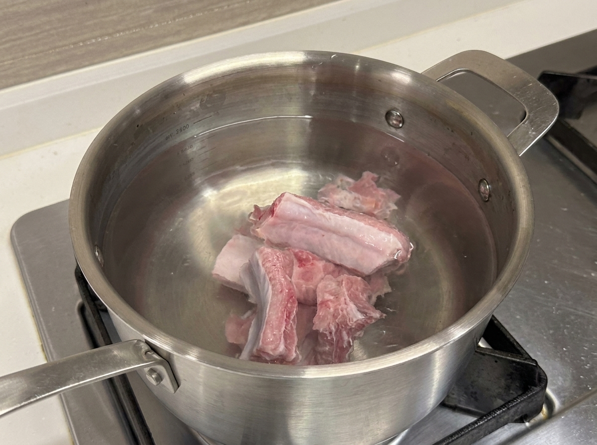 Travers de porc crus dans une marmite en inox remplie deau froide.