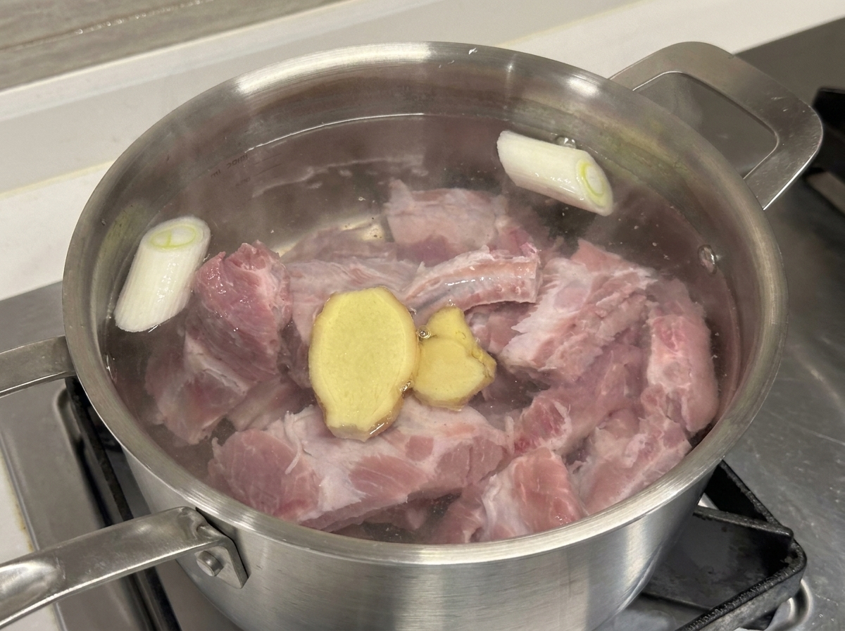 Marmite contenant les travers de porc, oignons verts et tranches de gingembre avec du vin de cuisine.