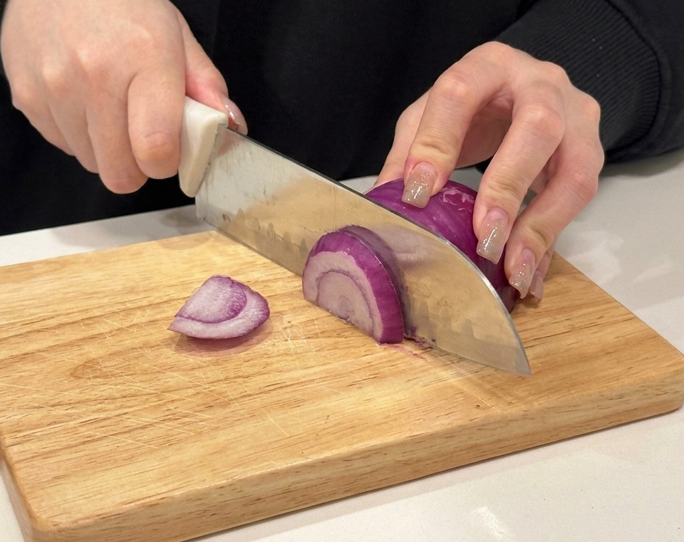 Mains tranchant un oignon rouge sur une planche à découper en bois.