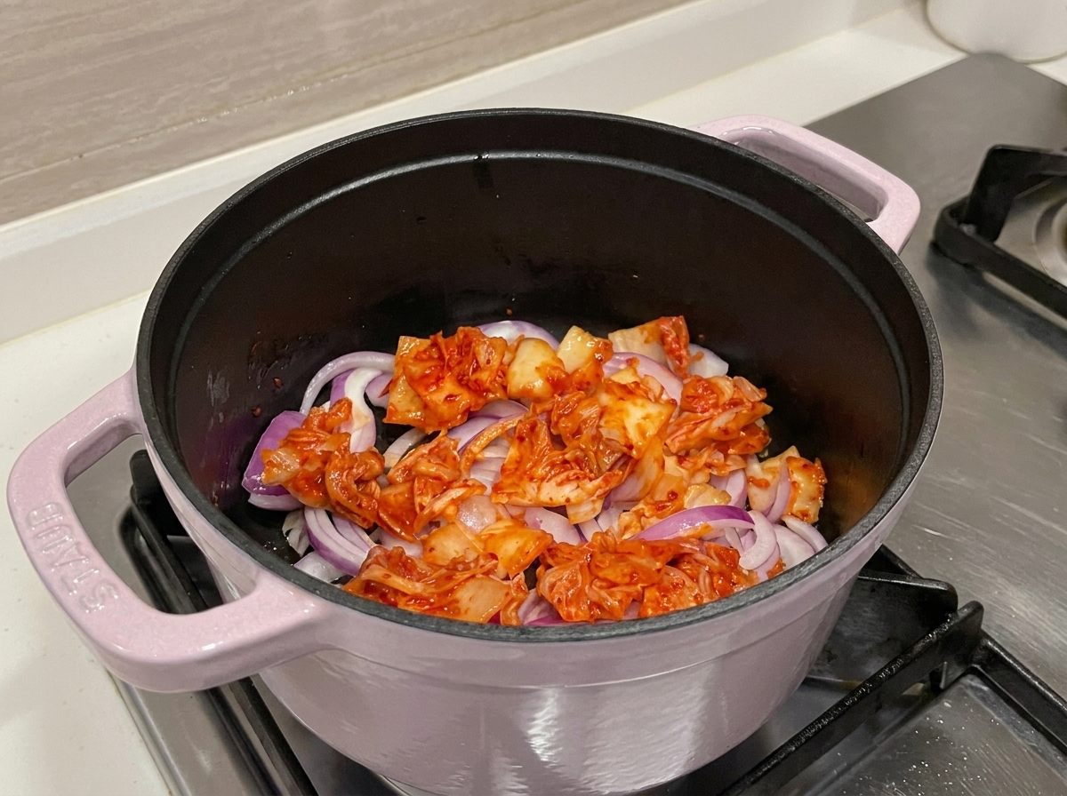 Vue rapprochée du kimchi rouge vif et des oignons sautant dans une marmite, libérant leurs sucs aromatiques.