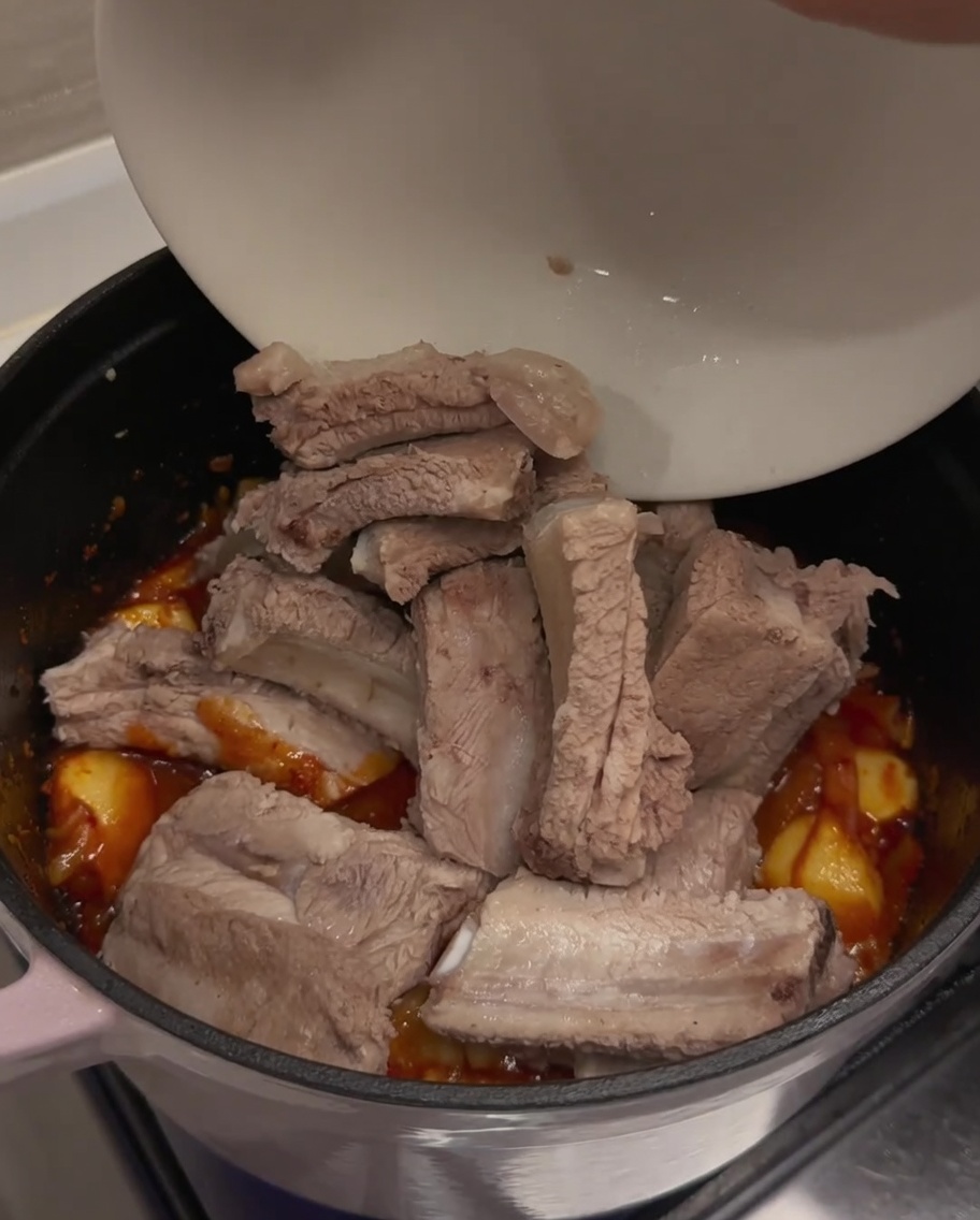 Travers de porc blanchis ajoutés depuis un bol blanc dans la marmite contenant la base de kimchi aromatique.
