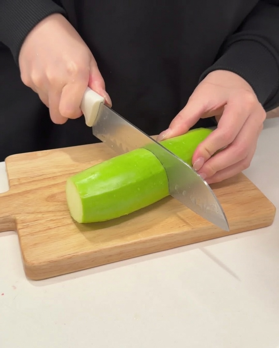 Un couteau tranchant une courgette verte ferme en demi-lunes sur une planche en bois.