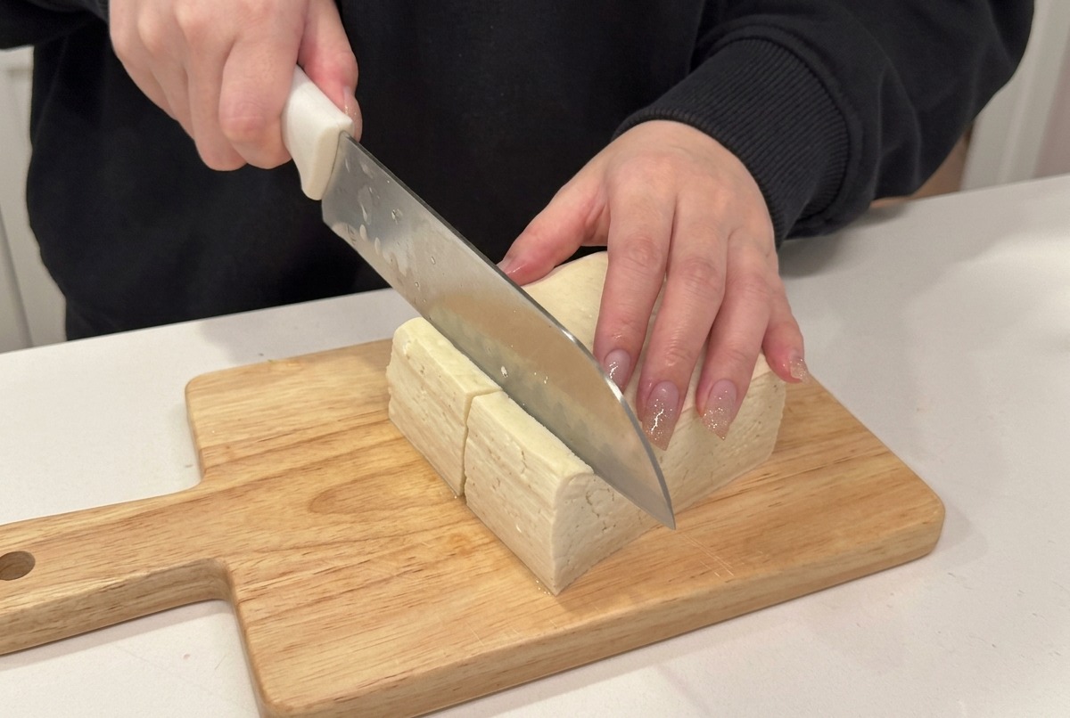 Gros plan dun couteau tranchant un bloc de tofu ferme en cubes sur une planche en bois.