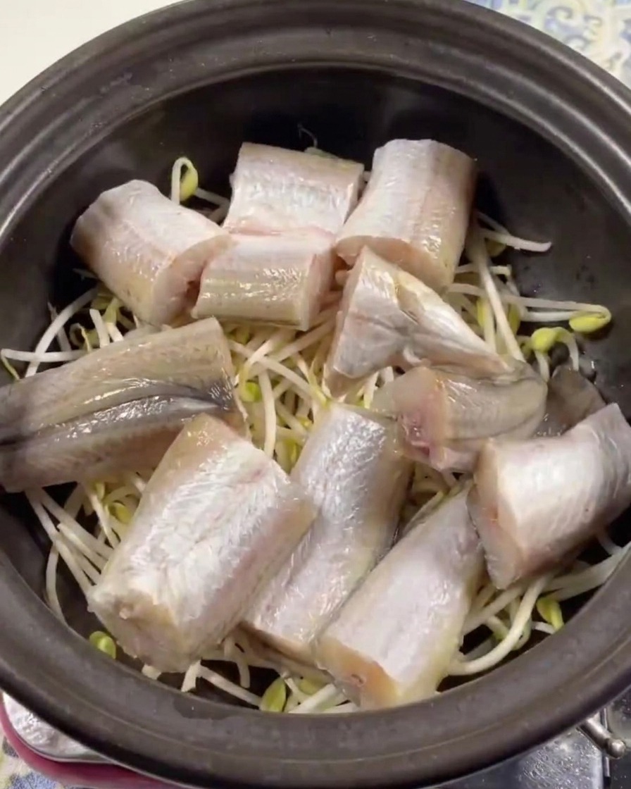 Morceaux de lieu jaune frais soigneusement disposés sur des pousses de soja dans une marmite en terre cuite foncée.