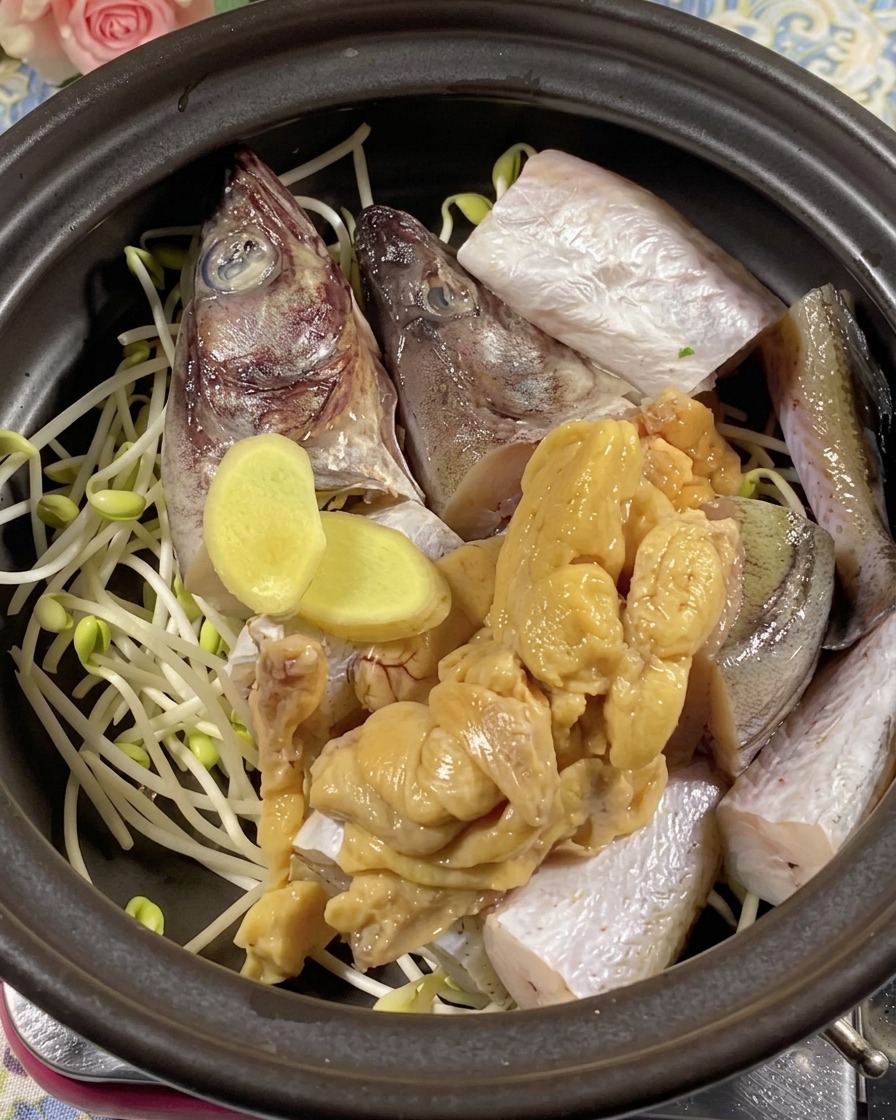 Tranches de gingembre frais et œufs de lieu jaune placés sur les morceaux de poisson dans une marmite.