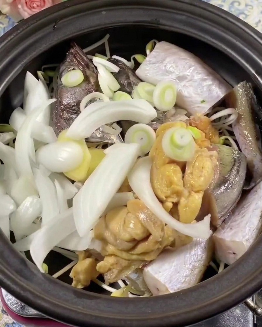 Gros plan sur des tranches de piment vert et rouge placées sur le poisson et les oignons dans la marmite.