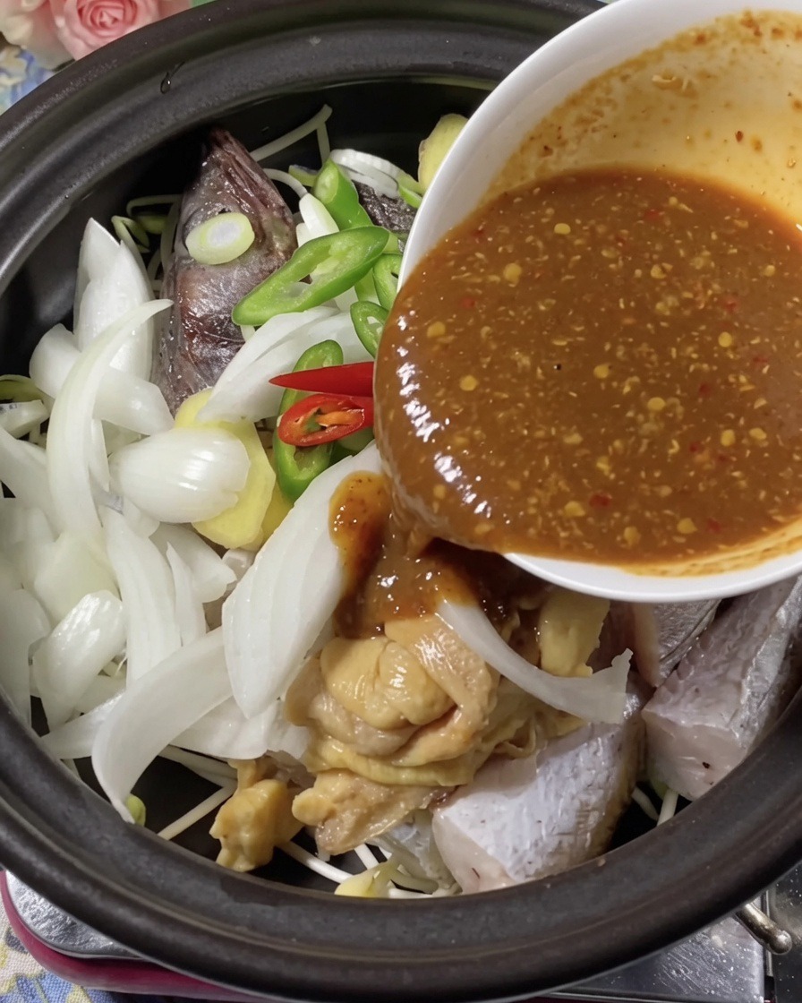 Une riche sauce dassaisonnement sombre versée depuis un bol sur le poisson et les aromates dans une marmite en terre cuite.